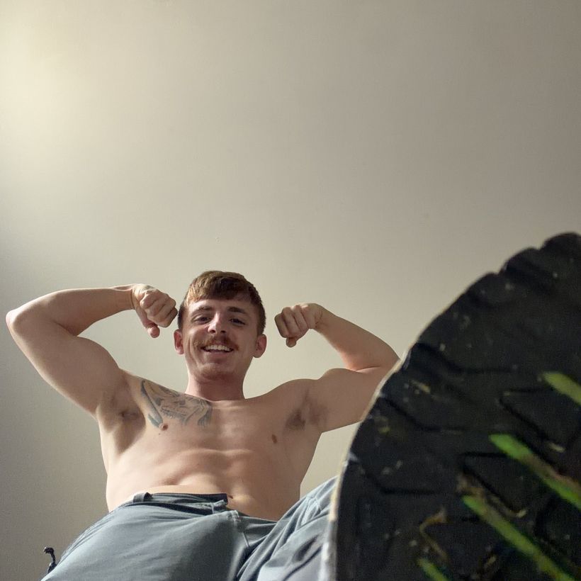Flexing both arms, grinning, a trainer sole in the foreground
